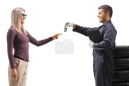 Téléchargez les photos : Mécanicien automobile avec un tas de pneus donnant des clés de voiture à une femme isolée sur fond blanc - en image libre de droit