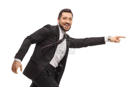 Téléchargez les photos : Homme souriant en costume noir courant et pointant isolé sur fond blanc - en image libre de droit