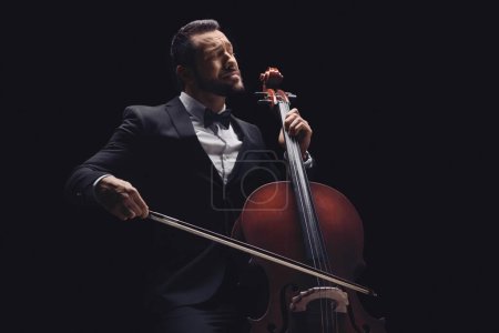 Photo for Male musician in a suit and bow-tie playing a cello over black background - Royalty Free Image