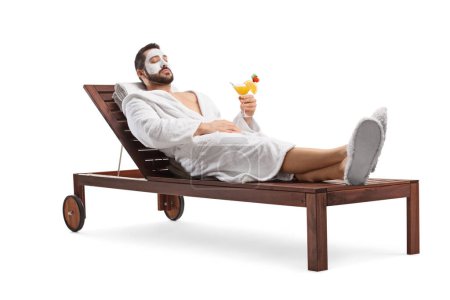 Foto de Hombre en un albornoz con una máscara facial descansando en una tumbona cubierta con un cóctel aislado sobre fondo blanco - Imagen libre de derechos