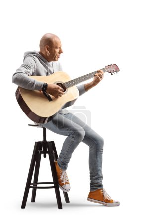Photo for Full length profile shot of a bald man playing an acoustic guitar seated on a chair isolated on white background - Royalty Free Image