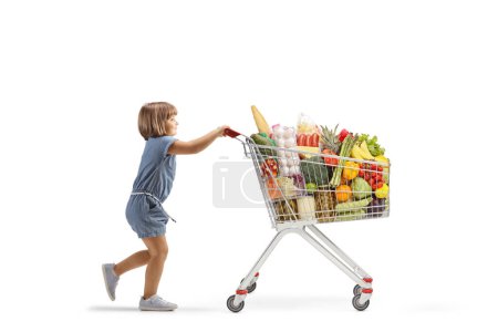 Foto de Imagen de perfil completo de una niña empujando un gran carrito de compras aislado sobre fondo blanco - Imagen libre de derechos