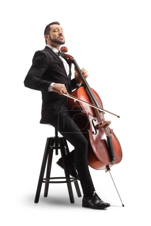 Photo for Male musician in a black suit and bow-tie sitting on a chair and playing a cello isolated on white background - Royalty Free Image