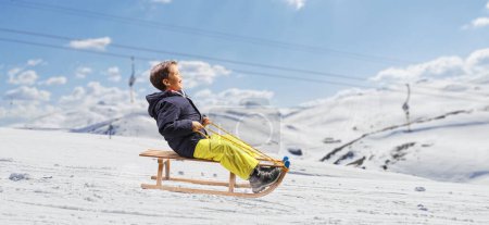 Photo for Boy sliding on a wooden sleigh at a ski resort - Royalty Free Image