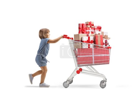 Foto de Foto de perfil completo de una niña empujando un gran carrito de compras con regalos aislados sobre fondo blanco - Imagen libre de derechos
