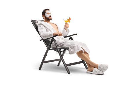 Foto de Hombre en un albornoz con una máscara facial sentado en la silla con un cóctel aislado sobre fondo blanco - Imagen libre de derechos