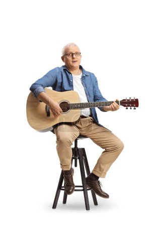 Foto de Hombre maduro con una guitarra acústica sentado en una silla y cantando aislado sobre fondo azul - Imagen libre de derechos