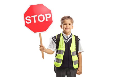 Téléchargez les photos : Écolier avec un gilet de sécurité et un panneau de signalisation d'arrêt regardant la caméra et souriant isolé sur fond blanc - en image libre de droit