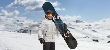 Photo for Happy young man holding a snowboard and looking at camera on a mountain - Royalty Free Image