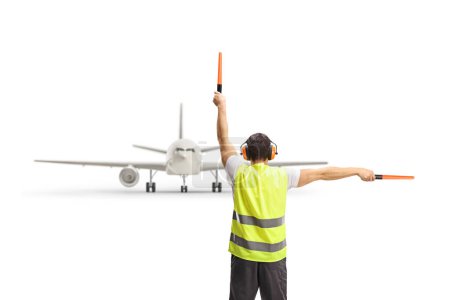 Foto de Rear view shot of a marshaller signalling with wands in front of an airplane isolated on white background - Imagen libre de derechos