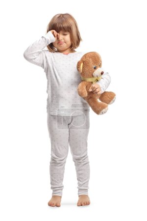 Photo for Child in pajamas holding a teddy bear and rubbing eyes isolated on white background - Royalty Free Image
