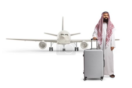 Foto de Full length portrait of a saudi arab man in a robe posing with a suitcase in front of an aircraft isolated on white background - Imagen libre de derechos