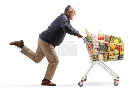 Foto de Excited mature man running with a shopping cart isolated on white background - Imagen libre de derechos