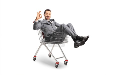 Photo pour Businessman sitting inside a shopping cart and gesturing good sign isolated on white background - image libre de droit