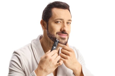 Foto de Man in a bathrobe using a beard trimmer isolated on white background - Imagen libre de derechos