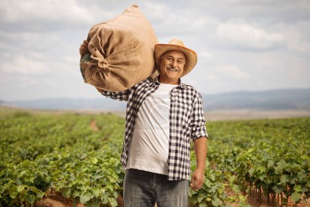 Photo for Farmer posing with a burlap sack on his shoulder on a grapevine field - Royalty Free Image