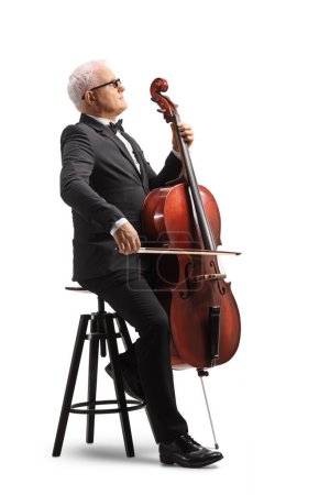 Photo for Profile shot of a mature musician sitting on a chair with a cello instrument isolated on white background - Royalty Free Image