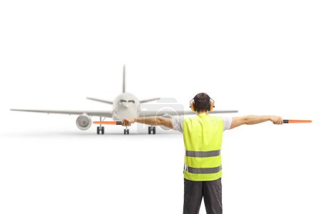Foto de Back view of an marshaller signalling with wands in front of an aircraft isolated on white background - Imagen libre de derechos