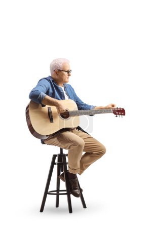 Foto de Mature man sitting on a chair playing an acoustic guitar  isolated on white background - Imagen libre de derechos