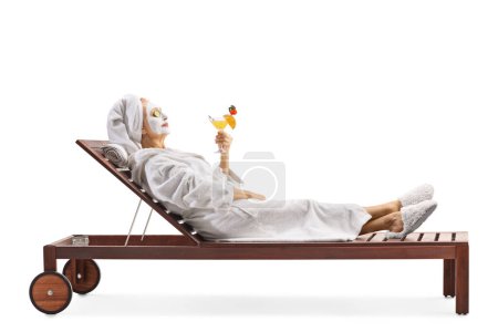 Téléchargez les photos : Woman in a bathrobe and hair wrapped in towel relaxing with a face mask and holding a cocktail isolated on white background - en image libre de droit