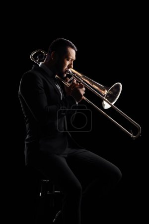 Photo for Man playing a trumpet and sitting on a chair isolated on black background - Royalty Free Image