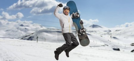 Téléchargez les photos : Happy man with a snowboard jumping and gesturing happiness on a snowy mountain - en image libre de droit