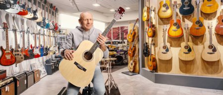 Téléchargez les photos : Guitarist sitting in a music store and holding an acoustic guitar - en image libre de droit