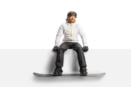 Foto de Man wearing a snowboard and sitting on a blank panel isolated on white background - Imagen libre de derechos