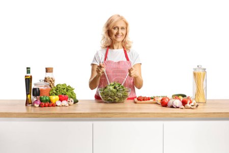 Photo for Woman with an apron preparing a salad on a kitchen counter isolated on white background - Royalty Free Image