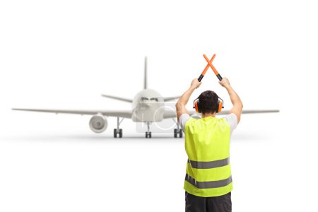 Foto de Rear view shot of a marshaller signalling with crossed wands in front of an aircraft isolated on white background - Imagen libre de derechos