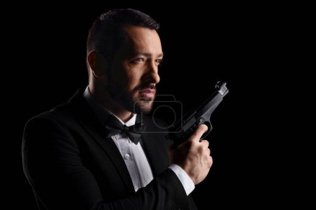 Téléchargez les photos : Man with a bow tie holding a gun isolated over black background - en image libre de droit