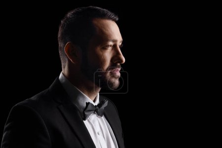 Foto de Close up profile shot of a man in a black suit and bow tie isolated over black background - Imagen libre de derechos