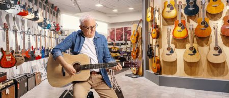 Téléchargez les photos : Mature man playing an acoustic guitar inside a music store - en image libre de droit
