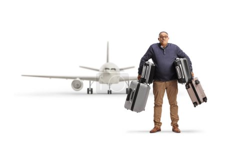Foto de Confused mature man carrying heavy suitcases in front of an airplane isolated on white background - Imagen libre de derechos