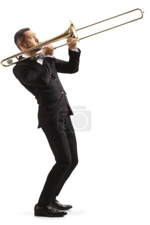 Photo for Full length profile shot of a man in a black suit playing a trombone isolated on white background - Royalty Free Image