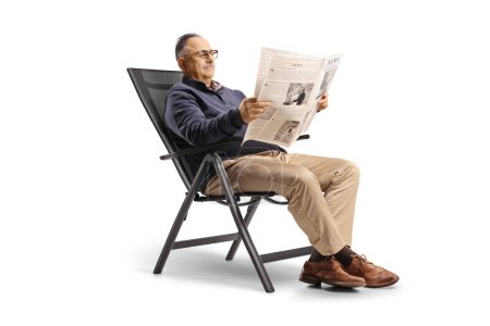 Foto de Casual mature man sitting in a foldable chair and reading a newspaper isolated on white background - Imagen libre de derechos