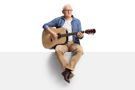 Téléchargez les photos : Mature man playing an acoustic guitar and sitting on a blank panel isolated on white background - en image libre de droit