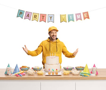 Foto de Guy gesturing with hands behind a counter with party snacks and a cake isolated on white background - Imagen libre de derechos