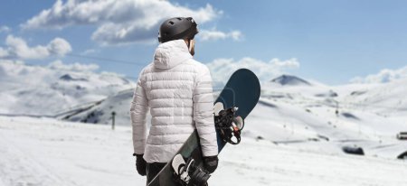 Foto de Rear view shot of a man holding a snowboard and looking at a mountain - Imagen libre de derechos