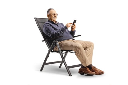Photo for Casual mature man sitting at a foldable chair and using a smartphone isolated on white background - Royalty Free Image