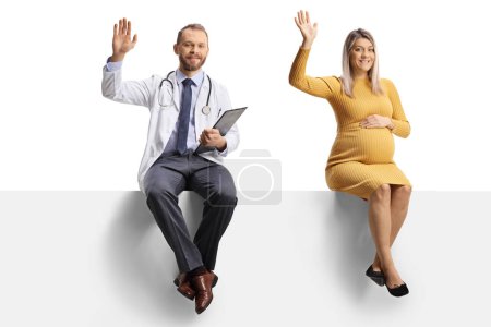 Photo for Male doctor and a pregnant woman sitting on a blank panel and waving at camera isolated on white background - Royalty Free Image