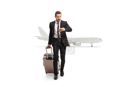 Photo for Full length portrait of a businessman with a suitcase checking his watch and getting off an airplane isolated on white background - Royalty Free Image