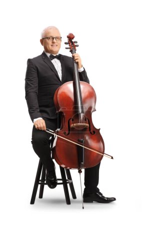 Photo for Full length portrait of a musician in a black suit and bow-tie sitting on a chair with a cello and smiling isolated on white background - Royalty Free Image