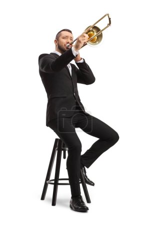 Photo for Male musician sitting on a chair and playing a trombone  isolated on white background - Royalty Free Image