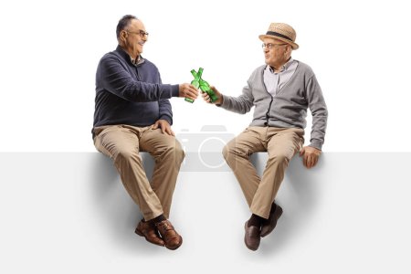 Téléchargez les photos : Cheerful male pensioners sitting on a blank panel with bottles of beer isolated on white background - en image libre de droit