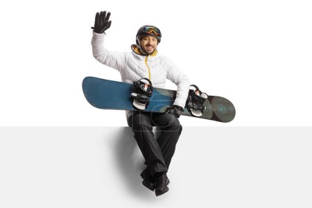 Téléchargez les photos : Man in a white jacket with a snowboard waving and sitting on a blank panel isolated on white background - en image libre de droit