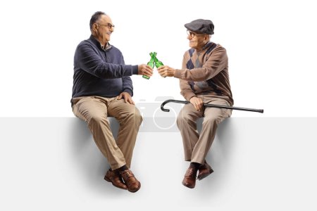 Foto de Cheerful elderly men sitting on a blank panel with bottles of beer isolated on white background - Imagen libre de derechos