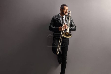 Photo for Young male trombone player standing and leaning on a grey wall - Royalty Free Image