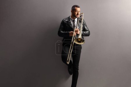 Photo for Young man with a trombone standing and leaning on a grey wall - Royalty Free Image