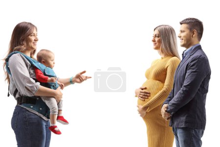 Téléchargez les photos : Profile shot of a mother with a baby in a carrier talking to a pregnant woman with her husband isolated on white background - en image libre de droit